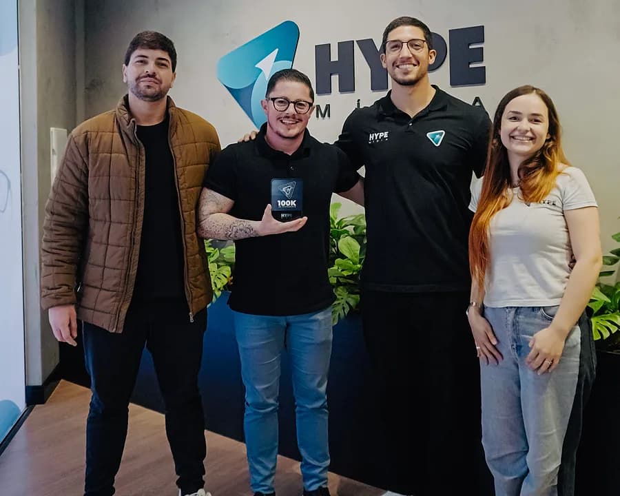 Quatro pessoas diante da marca na parede, uma delas segurando uma placa de marco de faturamento entregue a um cliente